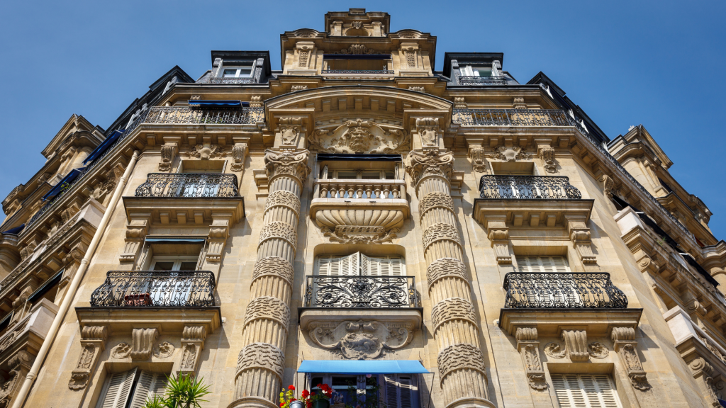 Ornate Haussmann-style apartment building facade in Paris with wrought-iron balconies, viewed from street level